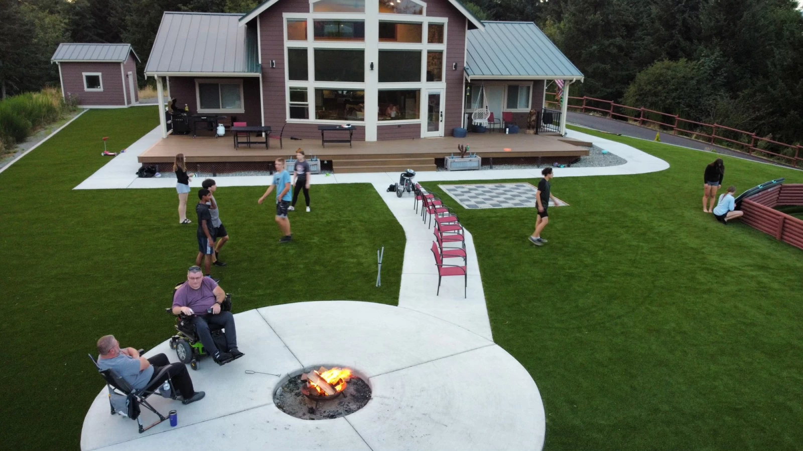 ADA compliant artificial turf installation with short pile height turf. Several kids playing on grass with adults hanging out by a fire.